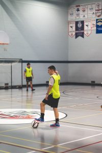 Men playing soccer indoors, showing teamwork and sport dynamics during practice session.