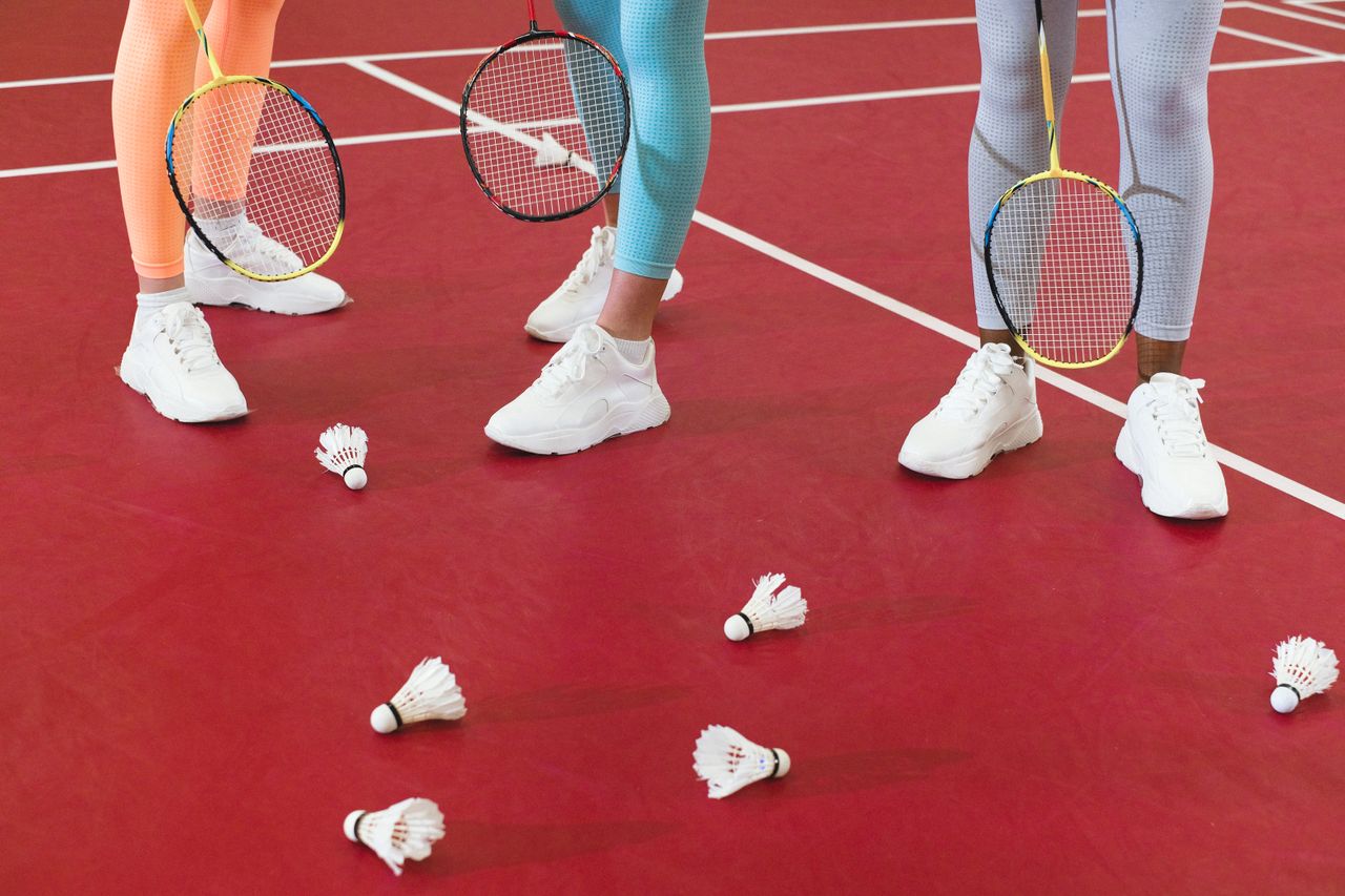 Crafting Captivating Headlines: Your awesome post title goes here Three badminton players with rackets and shuttlecocks on a red court wearing active wear.